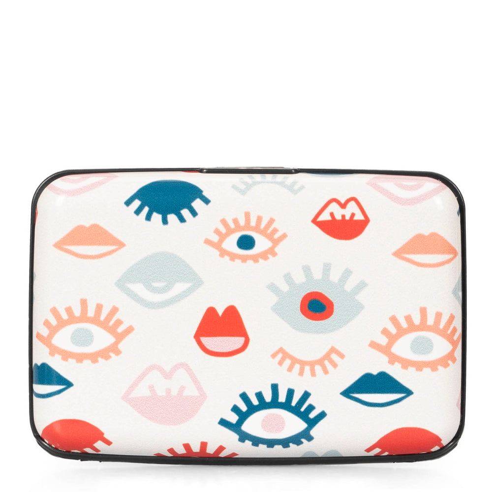 Back side of an aluminum card holder in a print of eye lashes and lips with white background showcasing black contour.